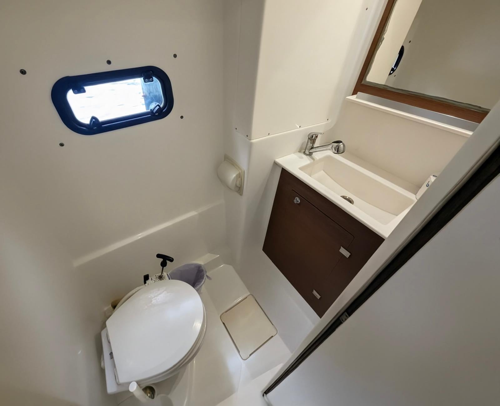 Yacht head with toilet, sink vanity, and porthole window